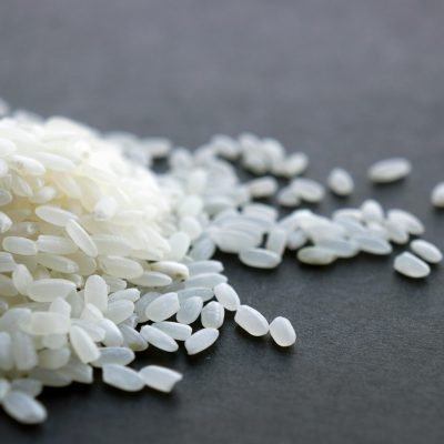 A close-up image showcasing a heap of fresh white rice grains on a dark surface.