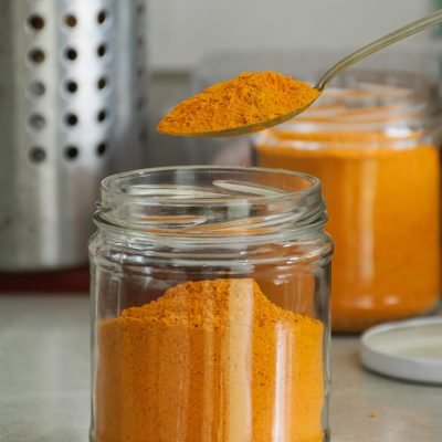 Close-up of bright turmeric powder in glass jars with spoon, enhancing culinary and health experiences.
