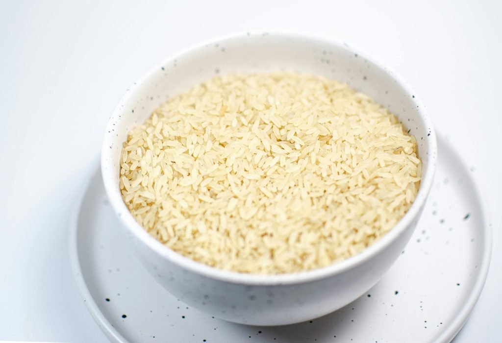 A close-up shot of uncooked rice grains in a speckled white bowl on a matching plate.