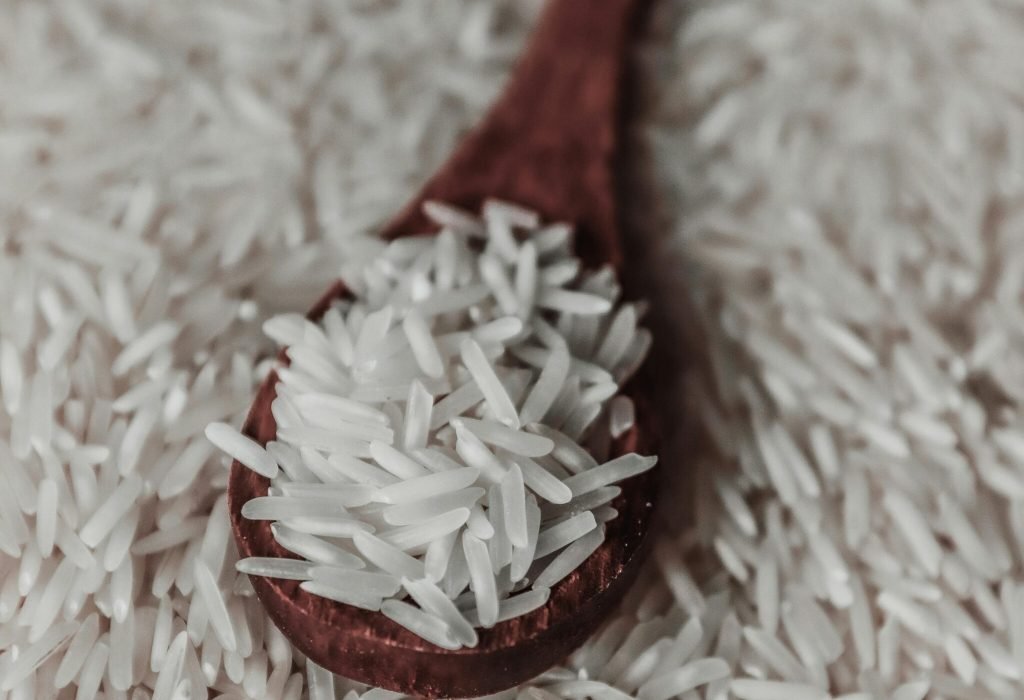 From above of raw white rice grains on wooden spoon placed on pile